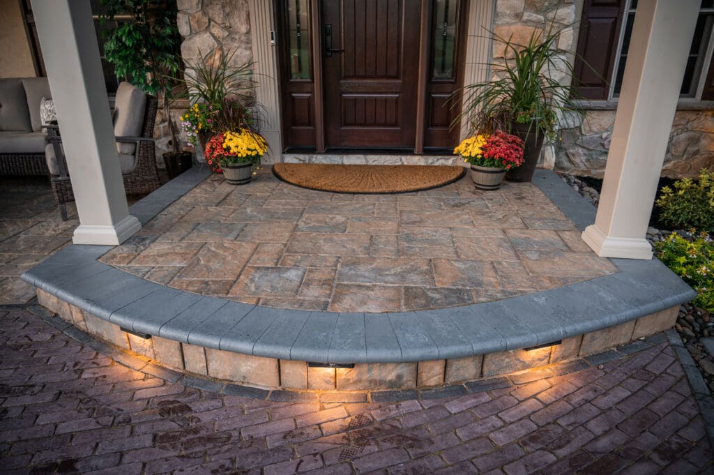 Paver entryway landing with welcome mat with potted plants and columns