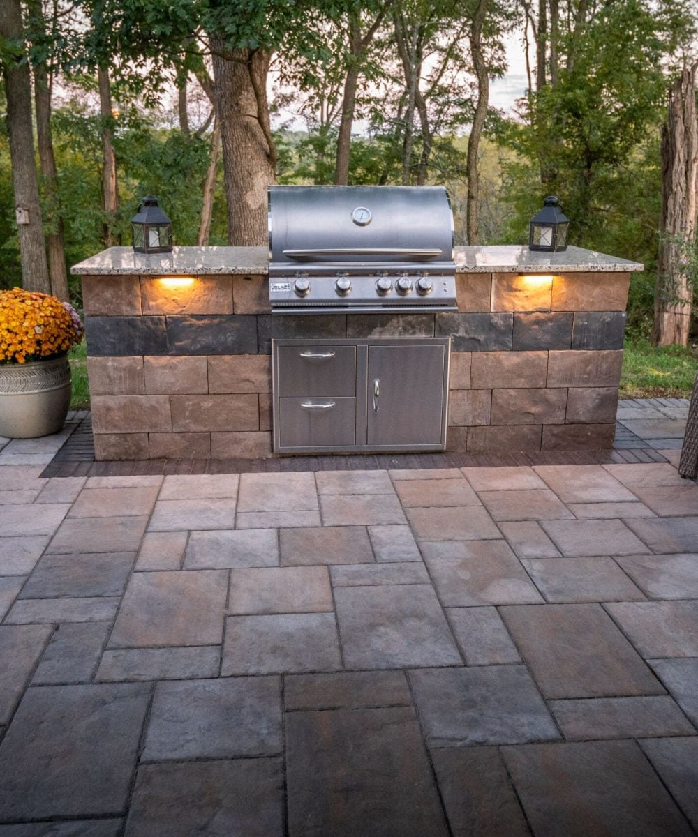 Outdoor grill station with built-in appliances and stone countertop, set on a patio with furniture next to it.